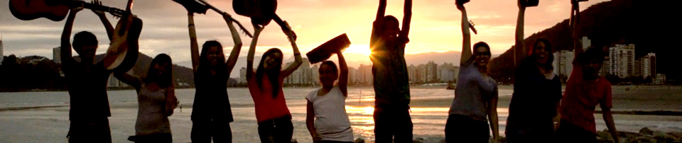 picture of the sunset on the beach with young men holding their instruments in the air in the foreground