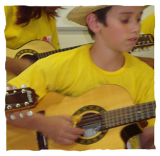 picture of a young boy dressing a yellow t-shirt of Guri, playing "viola caipira", similar to guitar